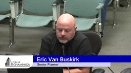 Eric VanBuskirk sits at presentation table with laptop open giving presentation. 
