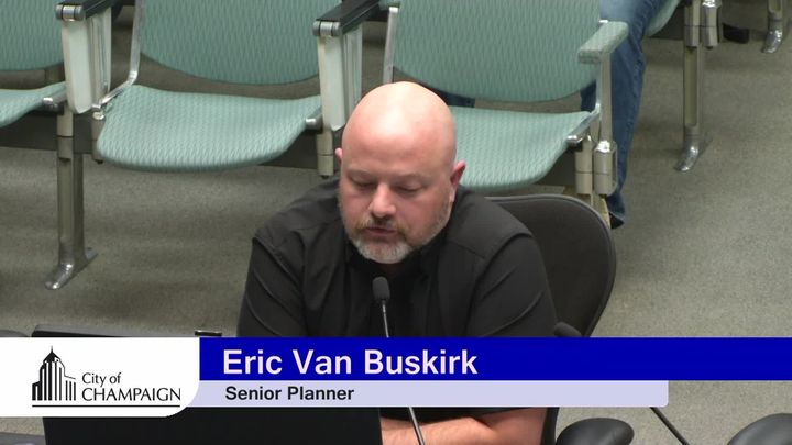 Eric VanBuskirk sits at presentation table with laptop open giving presentation. 