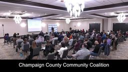 Wide shot from the back of the room of the audience, the presenter, and the presentation screen. 
